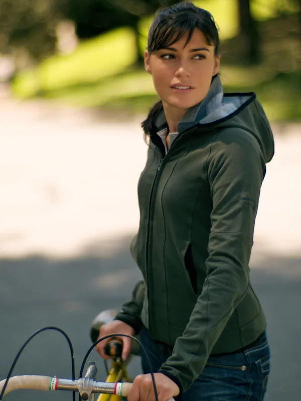 Personne en veste olive et jeans tenant un vélo dans un parc ensoleillé