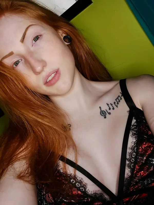 Portrait d'une personne aux cheveux roux, tatouage musical, tenue noire à dentelle, fond vert