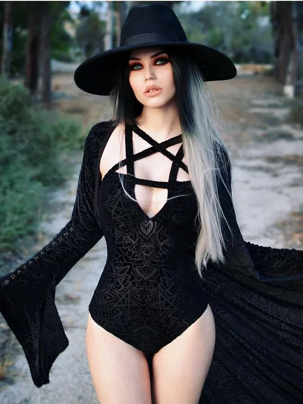 Personne en tenue noire avec chapeau large, cape et motifs, dans un cadre forestier.