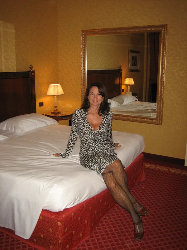 Personne en robe à motifs assise sur un lit dans une chambre d'hôtel, regardant l'appareil photo