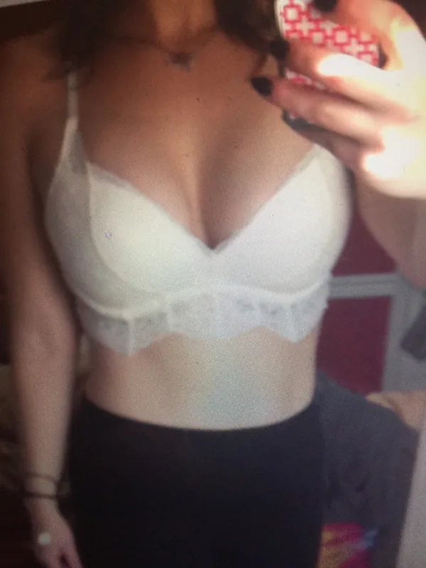 Portrait de femme en sous-vêtements blancs tenant un téléphone rose devant un miroir.