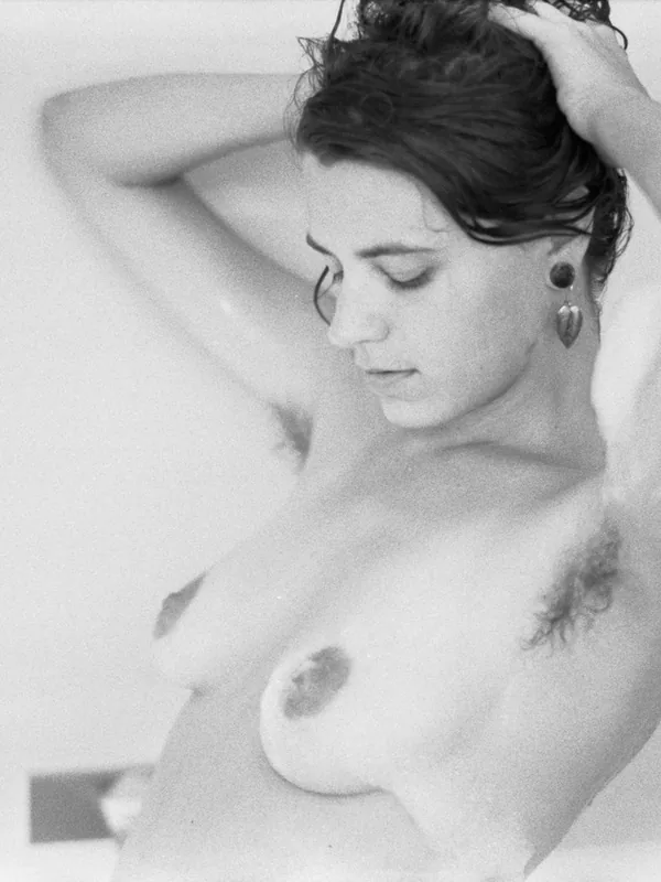 Portrait en noir et blanc d'une personne nue dans une baignoire, les mains dans les cheveux humides, regard baissé